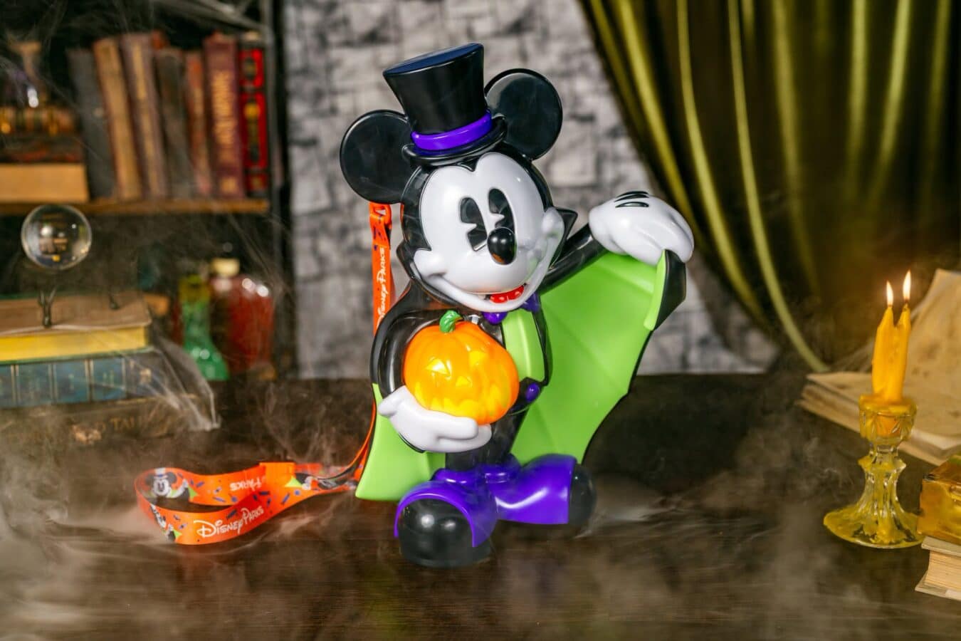 Disney Halloween display featuring Mickey Mouse holding an orange jack o lantern wearing a purple hat band and green outfit with candlelight nearby