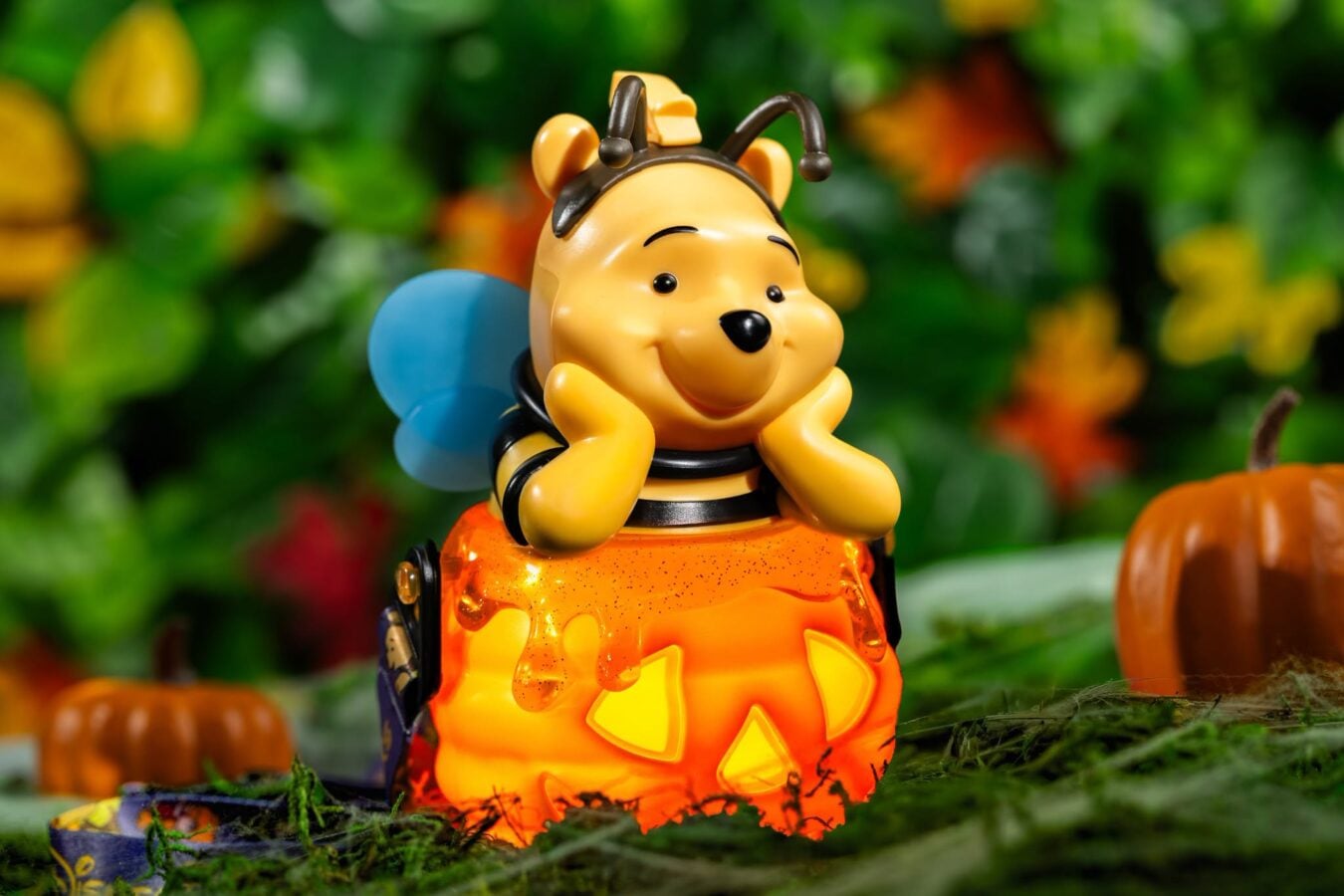 Smiling toy bee in an orange Halloween costume outdoors with pumpkins in the background