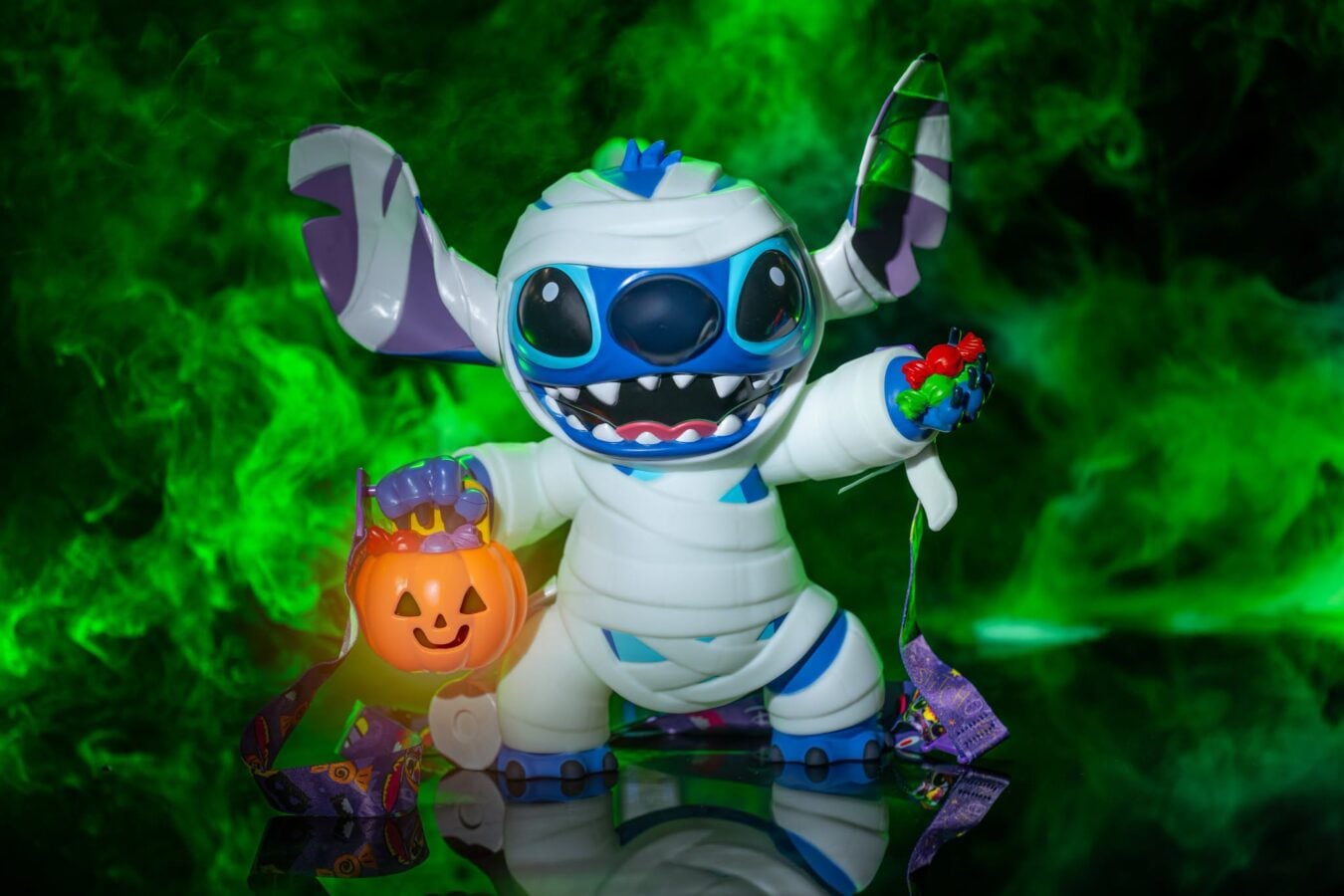 Costumed cartoon creature wearing a white suit with blue accents holding an orange pumpkin bucket and colorful candy against a green foggy background
