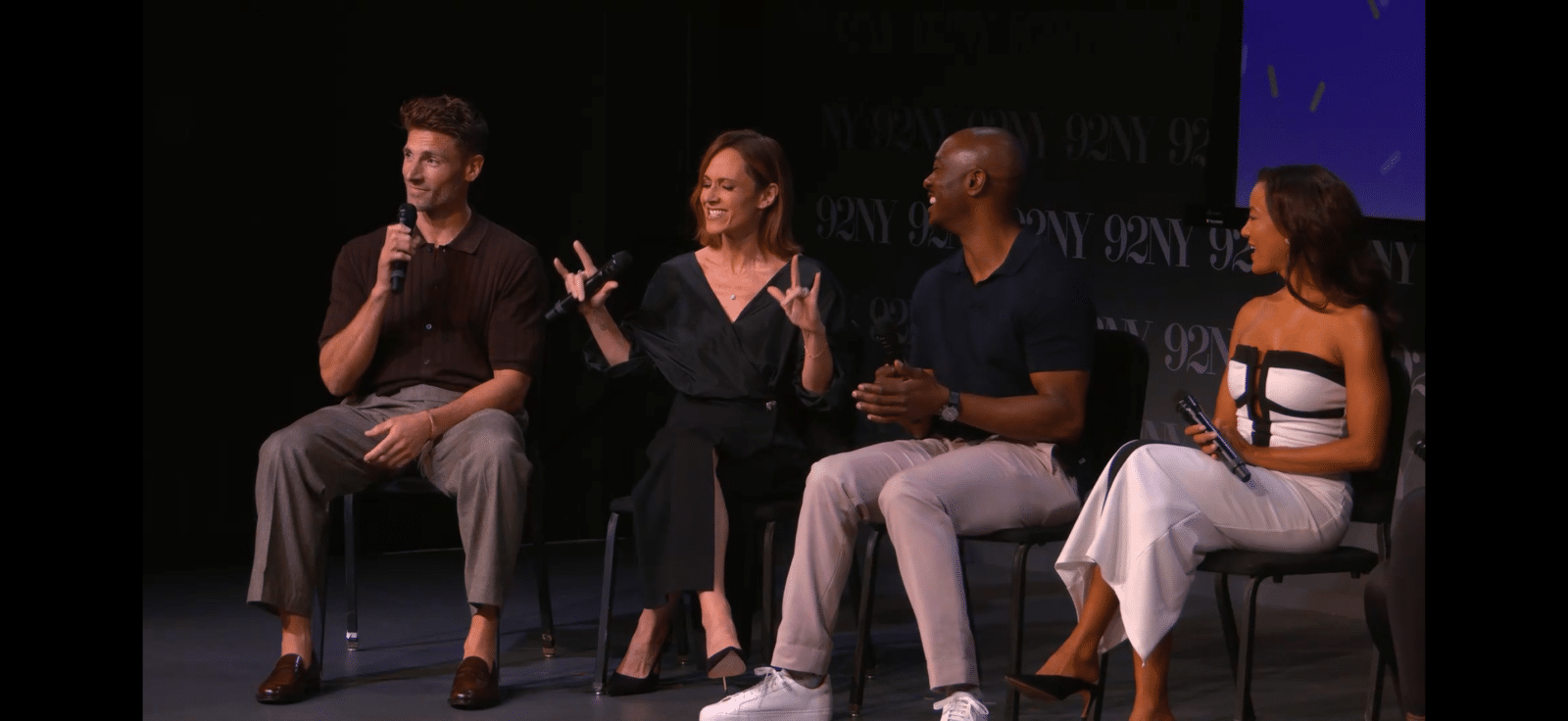 Four panelists seated on stage in discussion each holding a microphone engaging with one another