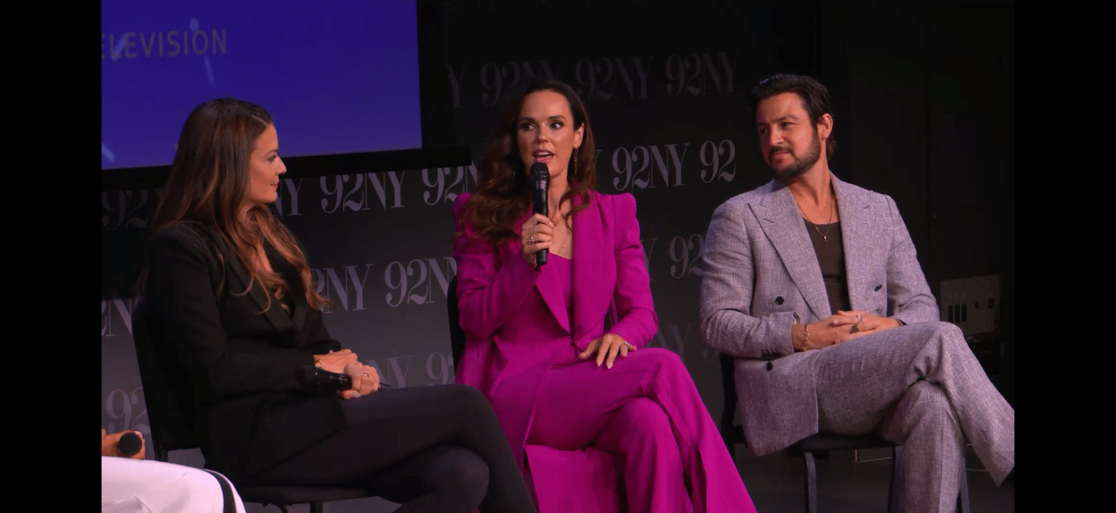 Three panelists seated on a stage center woman in magenta suit speaks into a microphone while the others listen with a 92Y backdrop behind them