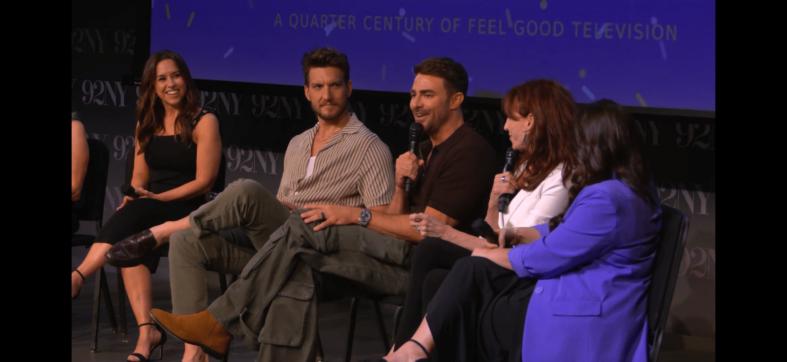 Panel of five people on a stage each holding a microphone during a discussion with a blue 92Y backdrop behind them