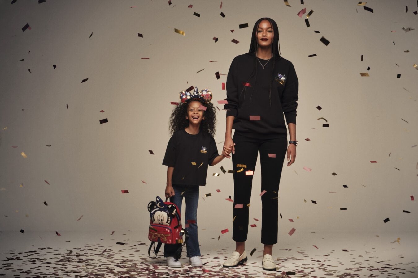 Adult and child stand hand in hand as confetti falls around them in a celebration photo