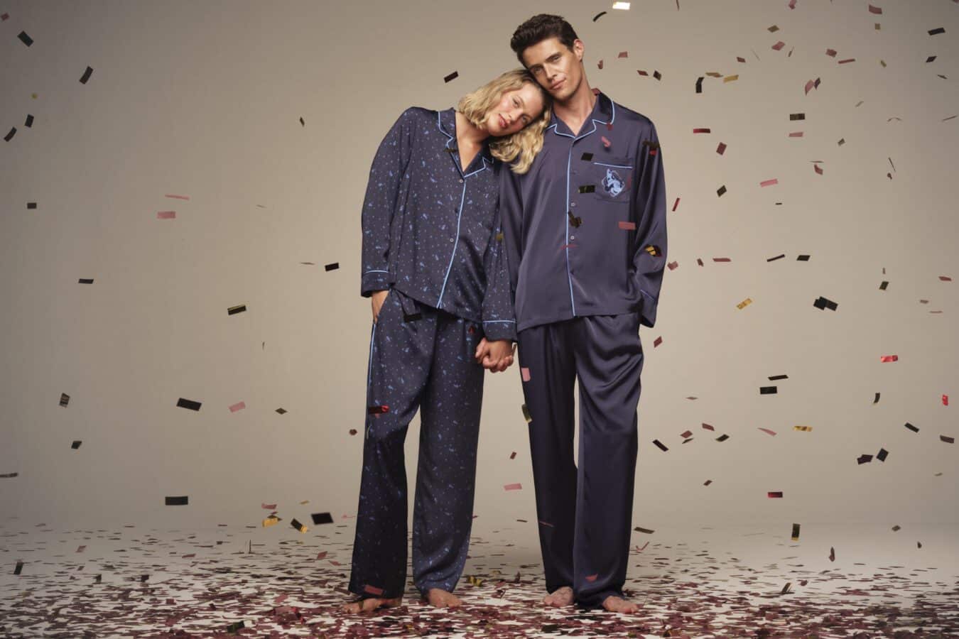 Couple in matching navy pajamas lean their heads together amid falling confetti posing for a celebratory shot
