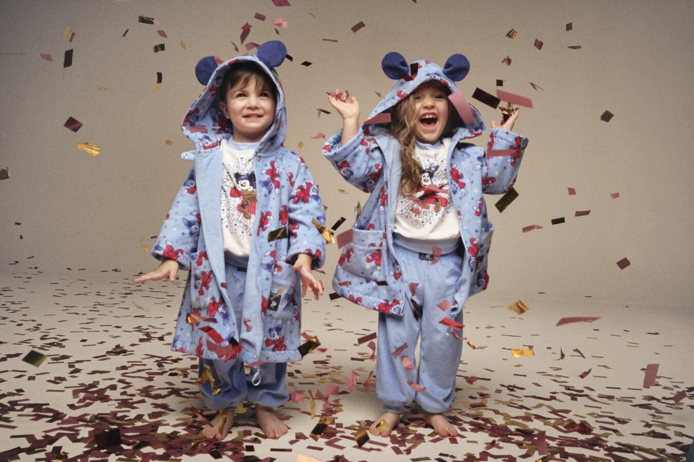 Two children in matching blue cartoon pajamas cheer as confetti falls around them