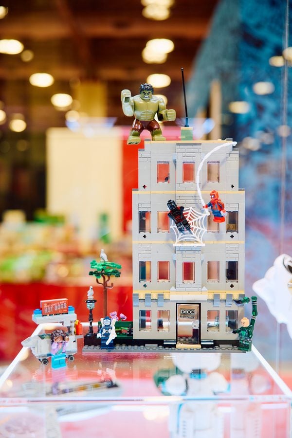 LEGO city scene with a tall gray building Hulk on the roof and Spider Man swinging on a web beside it