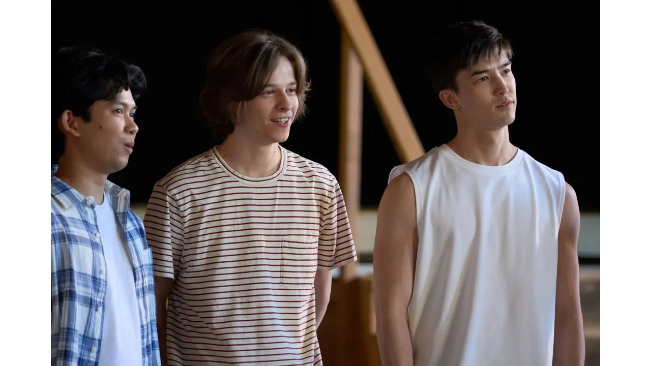 adty3 Fantasy Land News Three casually dressed young men stand side by side looking off to the right in a dim indoor setting