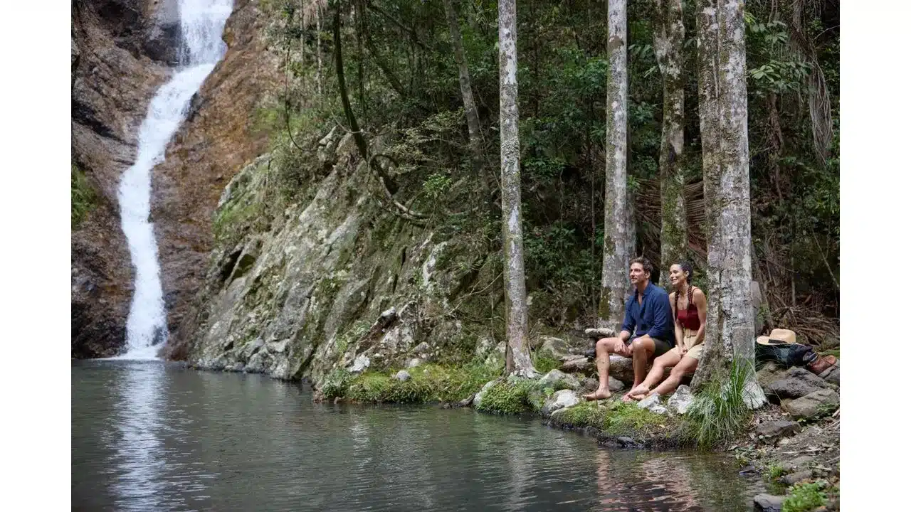 aussie1 Fantasy Land News Couple sitting on rocks by a forest waterfall feet in the water enjoying the scene