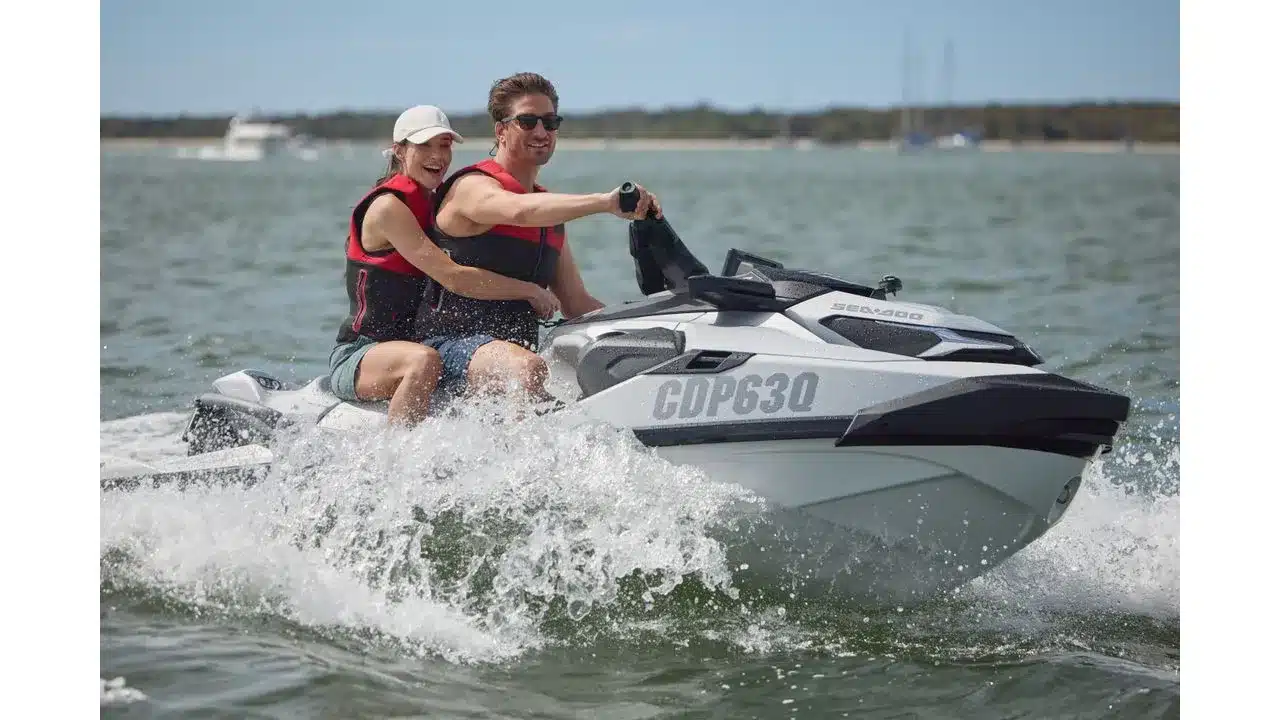 aussie2 Fantasy Land News Couple wearing red life jackets riding a white Sea Doo GP630 jet ski on the water spraying waves as they speed by