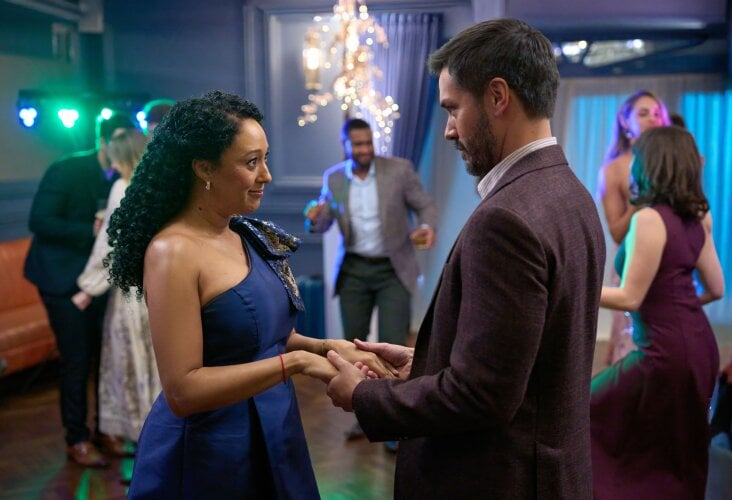 A couple dances while holding hands at a lively party with other guests in the background