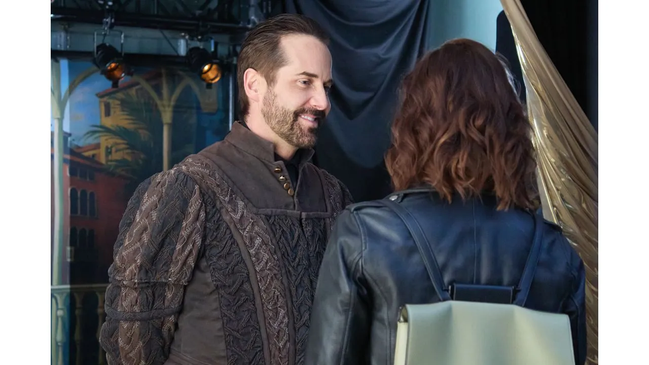 muchado1 Fantasy Land News Two adults in period costumes converse backstage on a theater set the man in a dark quilted tunic and the woman with a backpack seen from behind
