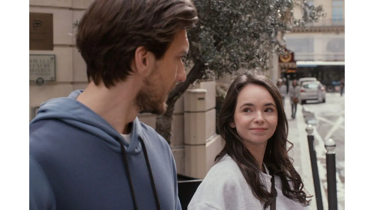 paris4b Fantasy Land News Man in a blue hoodie and a woman with long dark hair smile at each other while walking on a city sidewalk