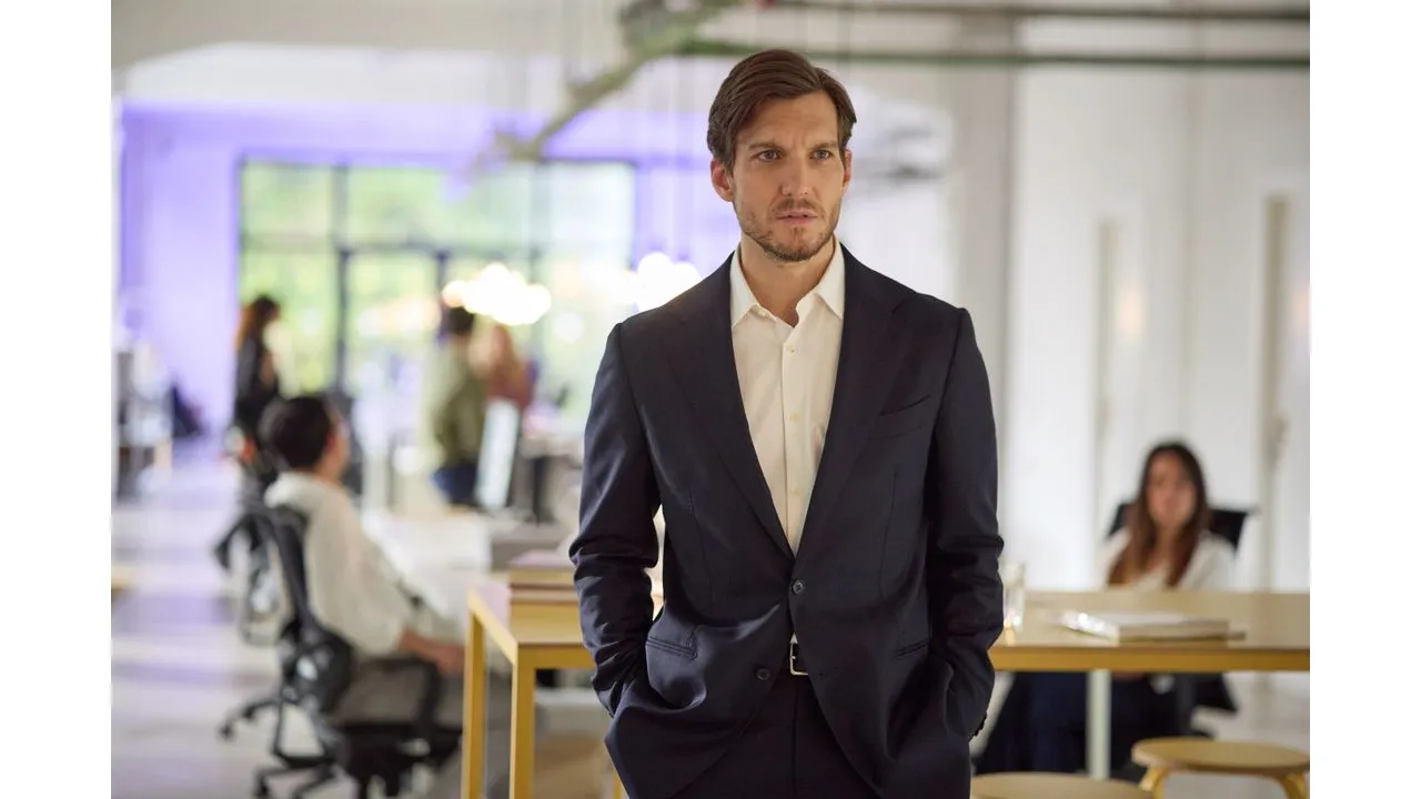 paris4e Fantasy Land News Professional man in a dark suit stands with hands in pockets in a modern open plan office coworkers blurred in the background