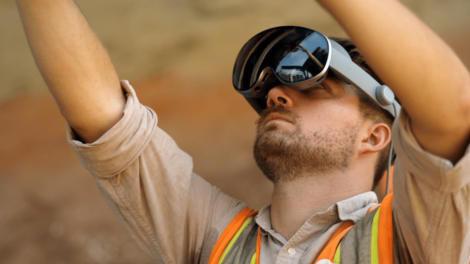 Construction worker wearing a VR headset with a reflective visor raising his arms outdoors safety vest visible