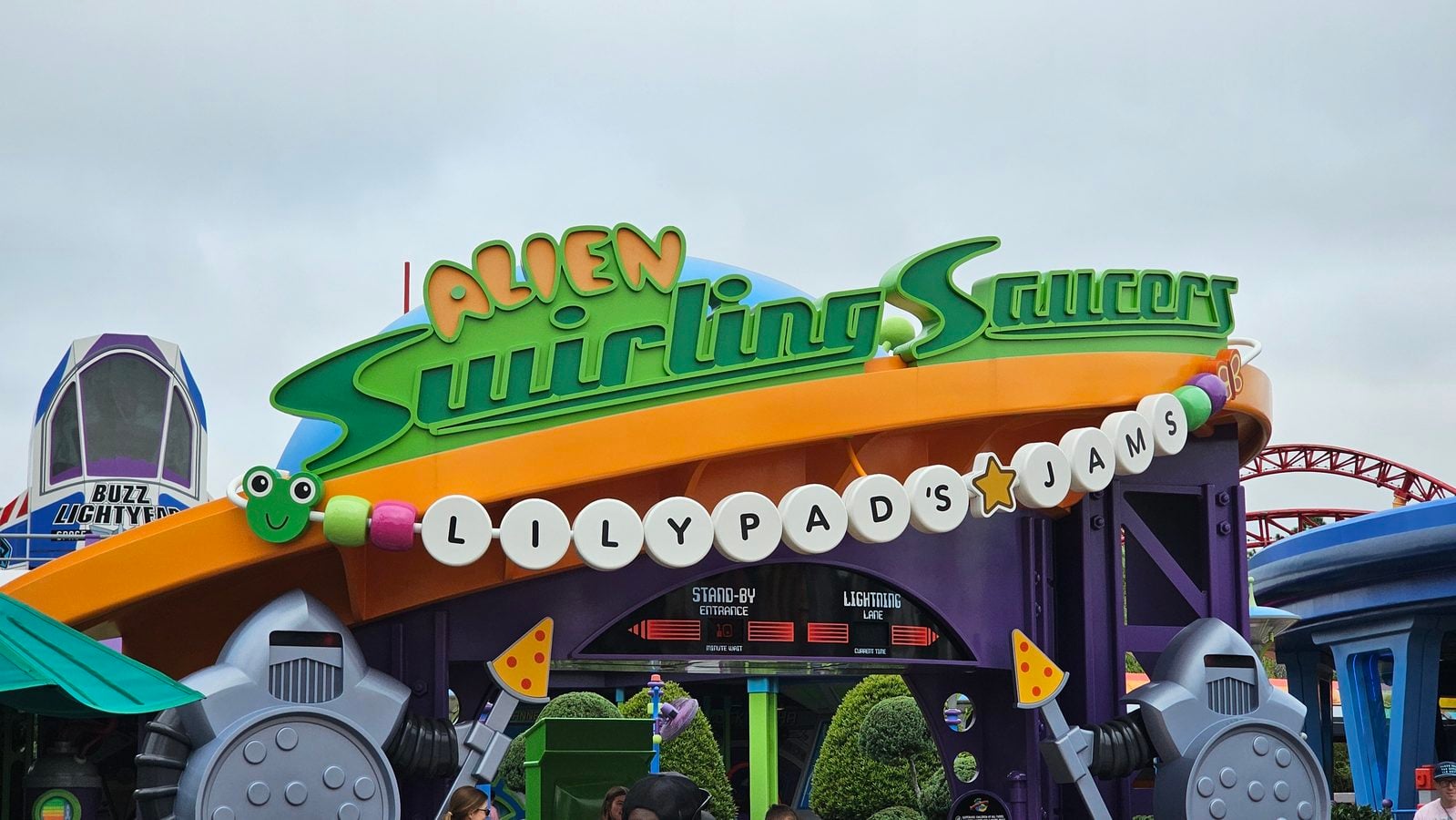 Colorful amusement park ride entrance with a bright green Lily Pads sign a smiling frog mascot and a curved orange track overhead