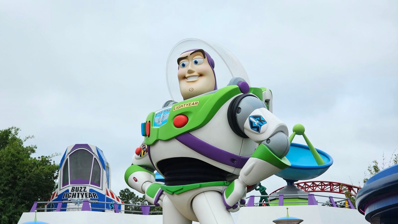 Life size Buzz Lightyear statue from Toy Story atop a colorful amusement park ride against a cloudy sky