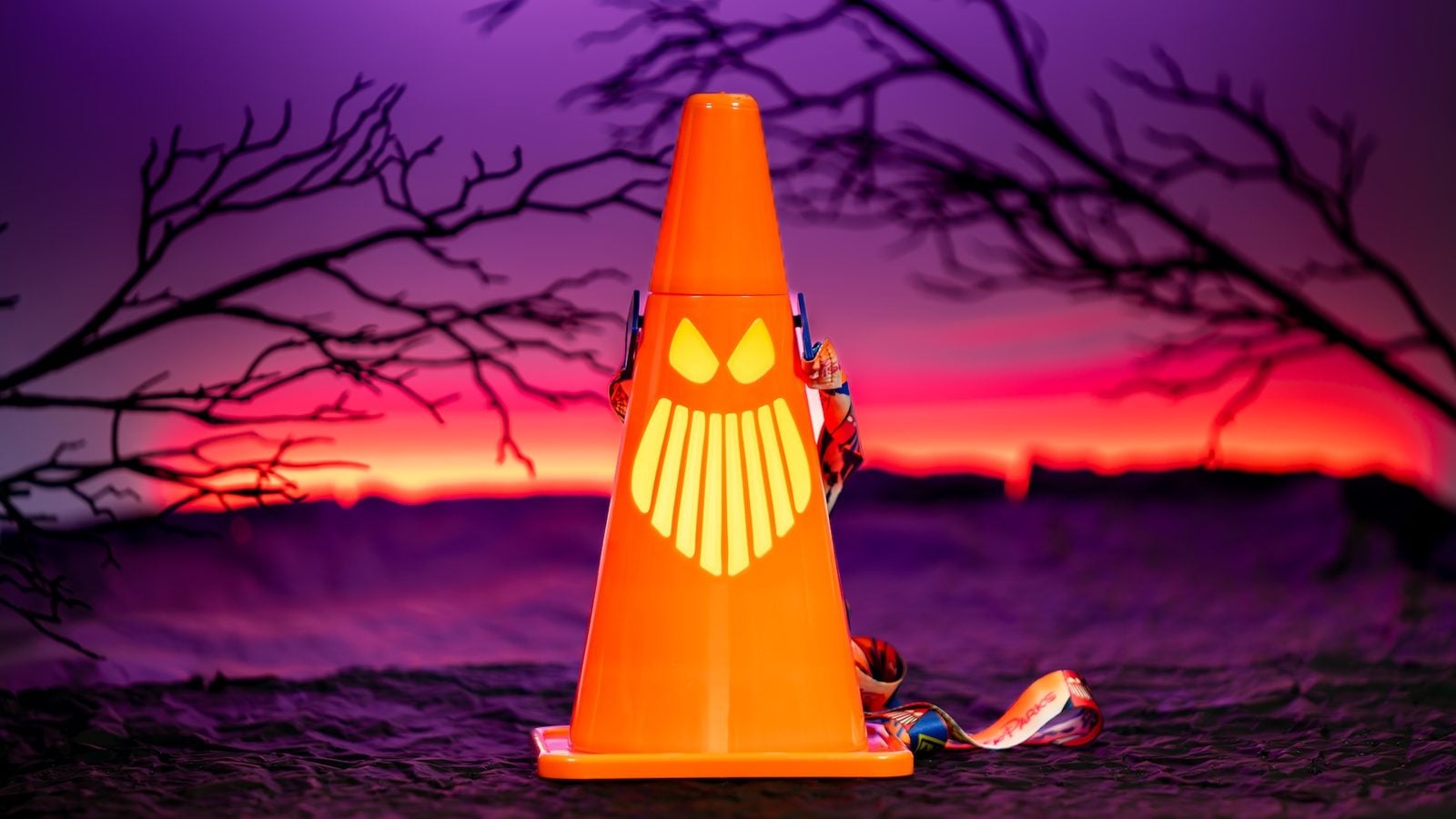 Orange traffic cone with a yellow face pattern in front of a purple orange sunset over water creating a Halloweeny scene