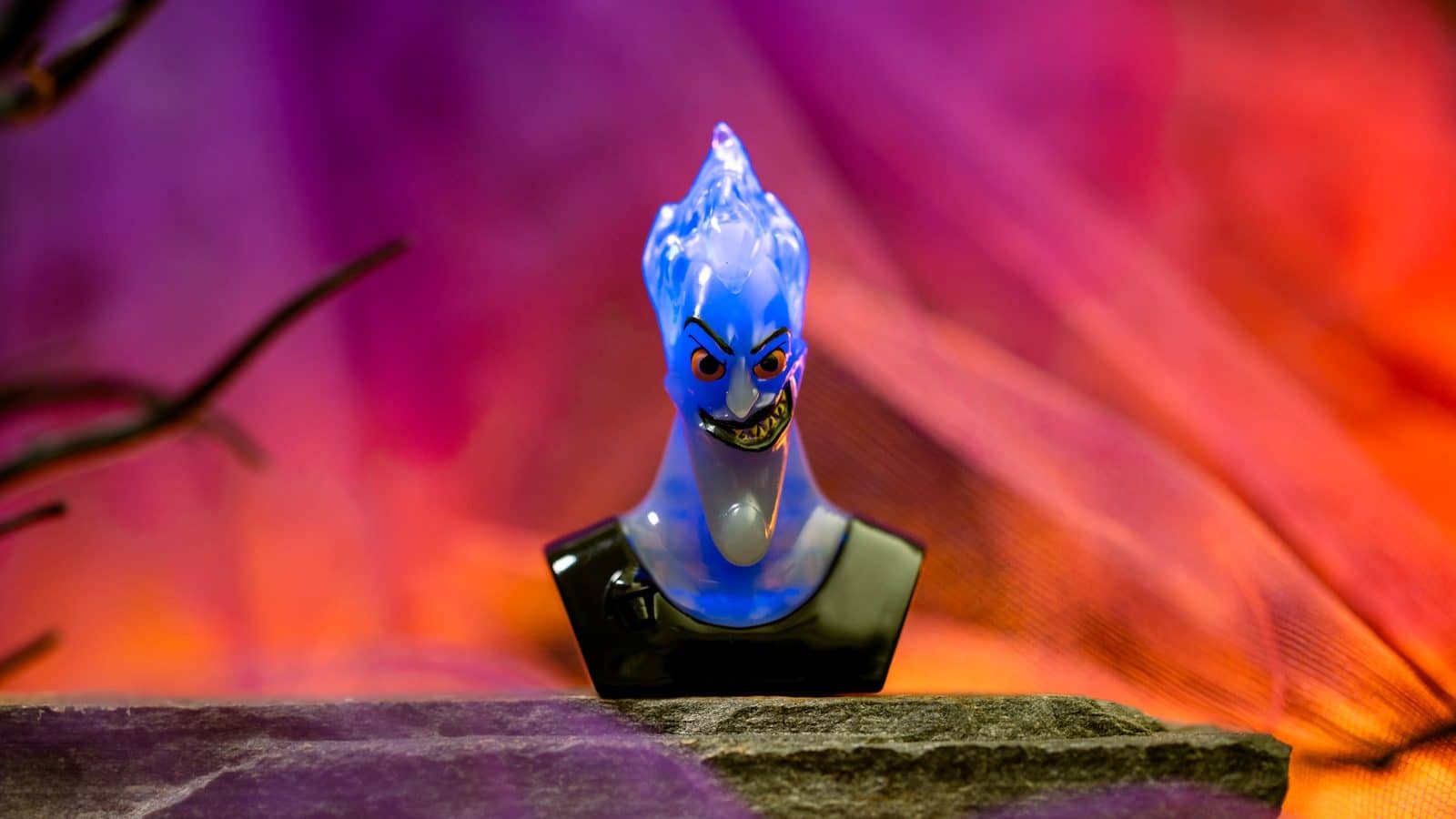 Blue cartoon bird toy with an angry expression standing on a stone ledge against a vibrant purpleorange background