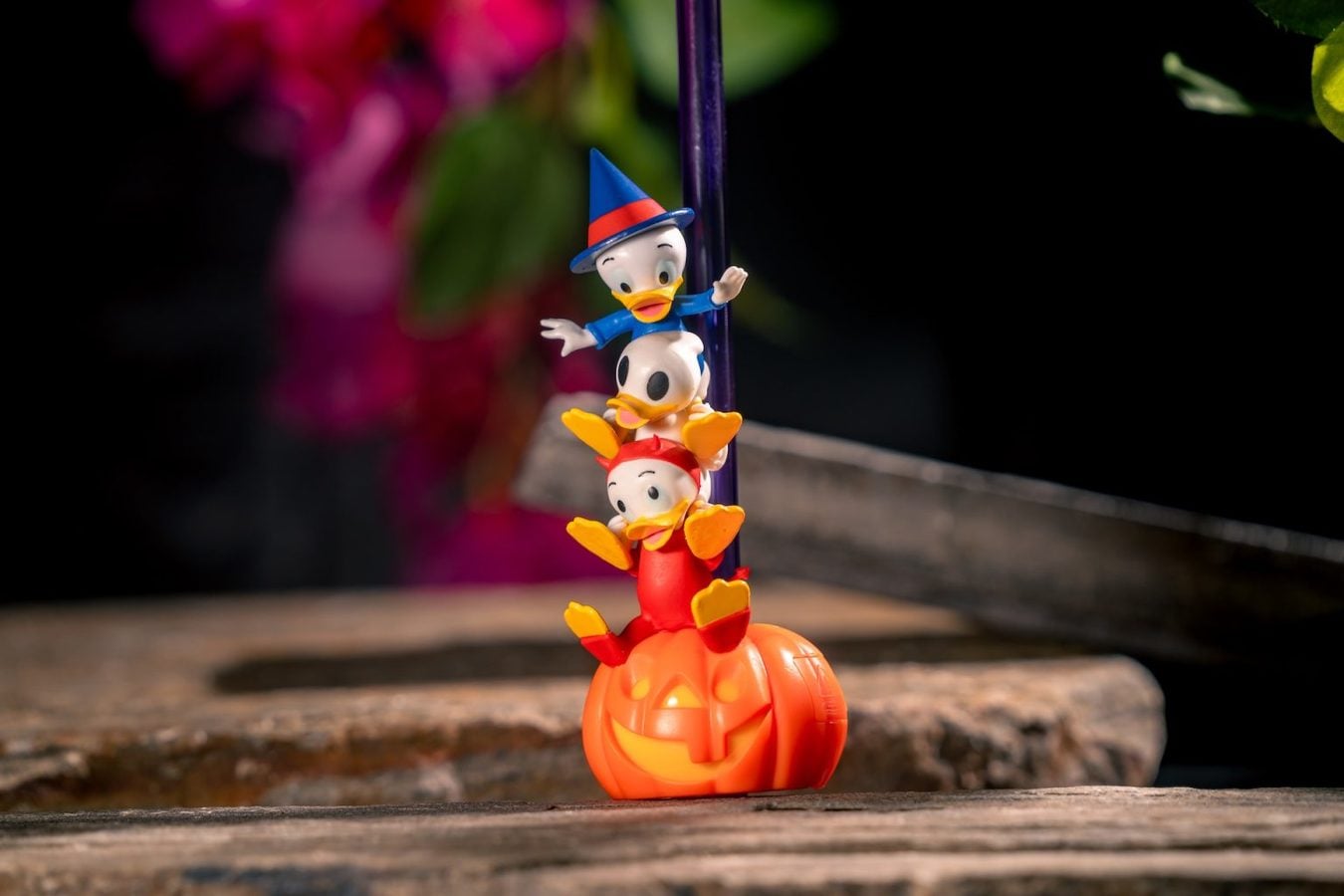 Three Disney duck figurines stacked on a carved orange pumpkin on a wooden surface outdoors