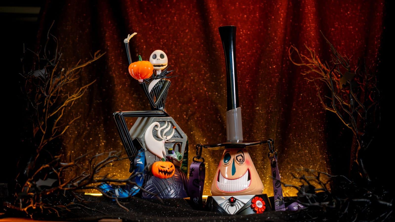 Halloween display with Jack Skellington holding a pumpkin atop a mechanical sculpture orange glittery backdrop and bare branches nearby