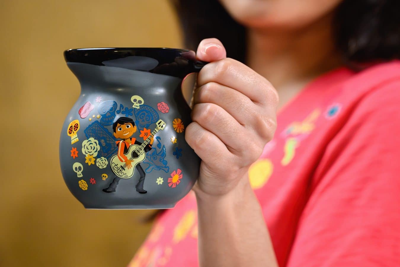 Close up of a childs hand gripping a blue mug covered with colorful stickers including skulls flowers and a guitarist image