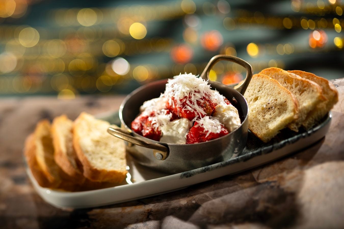 Small skillet with tomato and melted cheese topped with shredded cheese and slices of crusty bread nearby on a wooden table