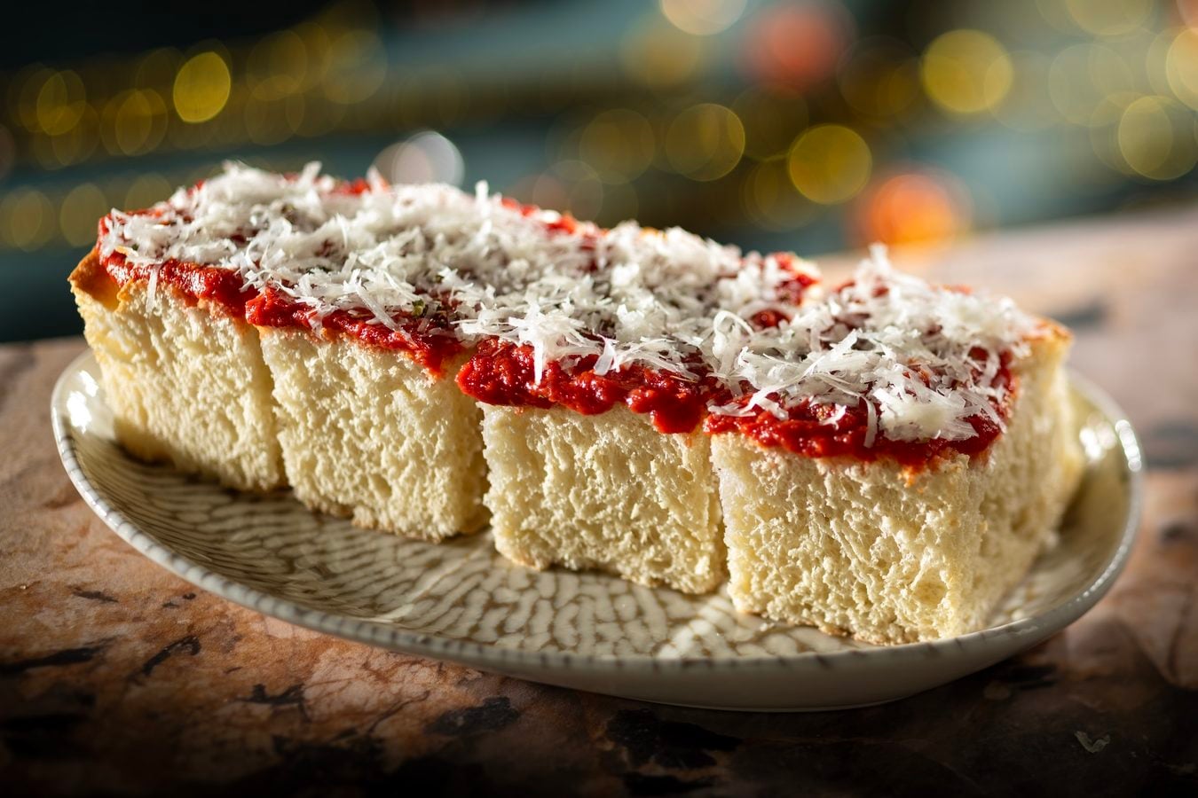 A slice of vanilla sponge cake topped with red jam and shredded coconut on a patterned plate