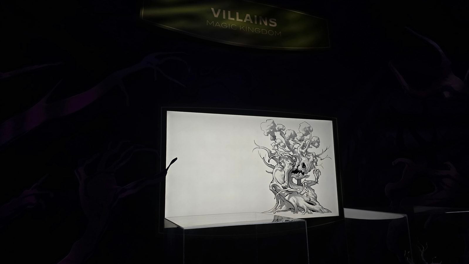Dim display case with a lit black and white drawing of a twisting tree like monster overhead banner reads VILLAINS MAGIC KINGDOM