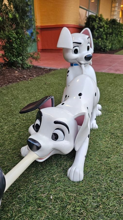 Two white Dalmatian statue dogs on a grassy area the foreground dog lies down with a bone in its mouth a second Dalmatian sits behind it
