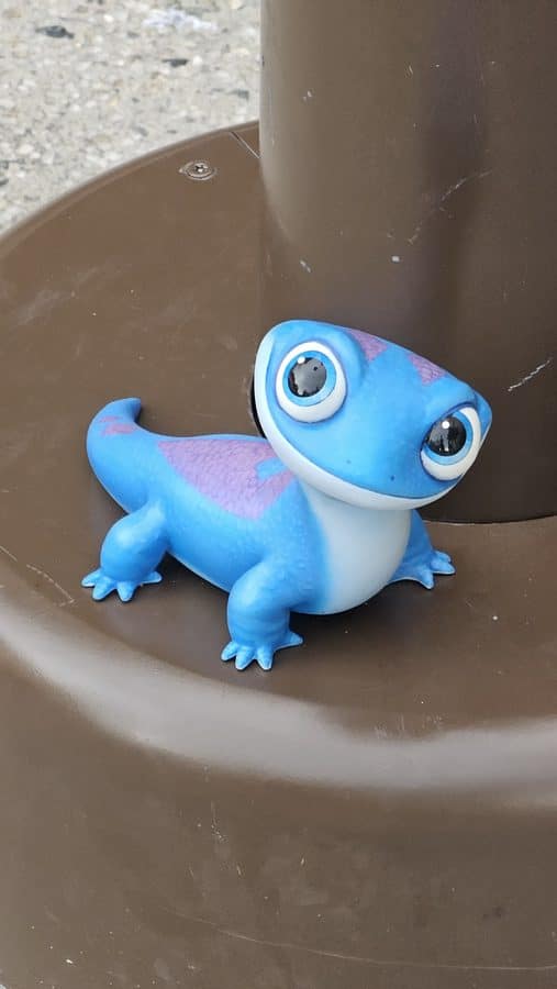 Blue cartoon frog toy with large eyes sits on a brown playground slide near the edge of the curve on a textured surface