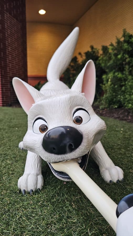 White cartoon dog statue on grass with a large bone in its mouth playful outdoor decor