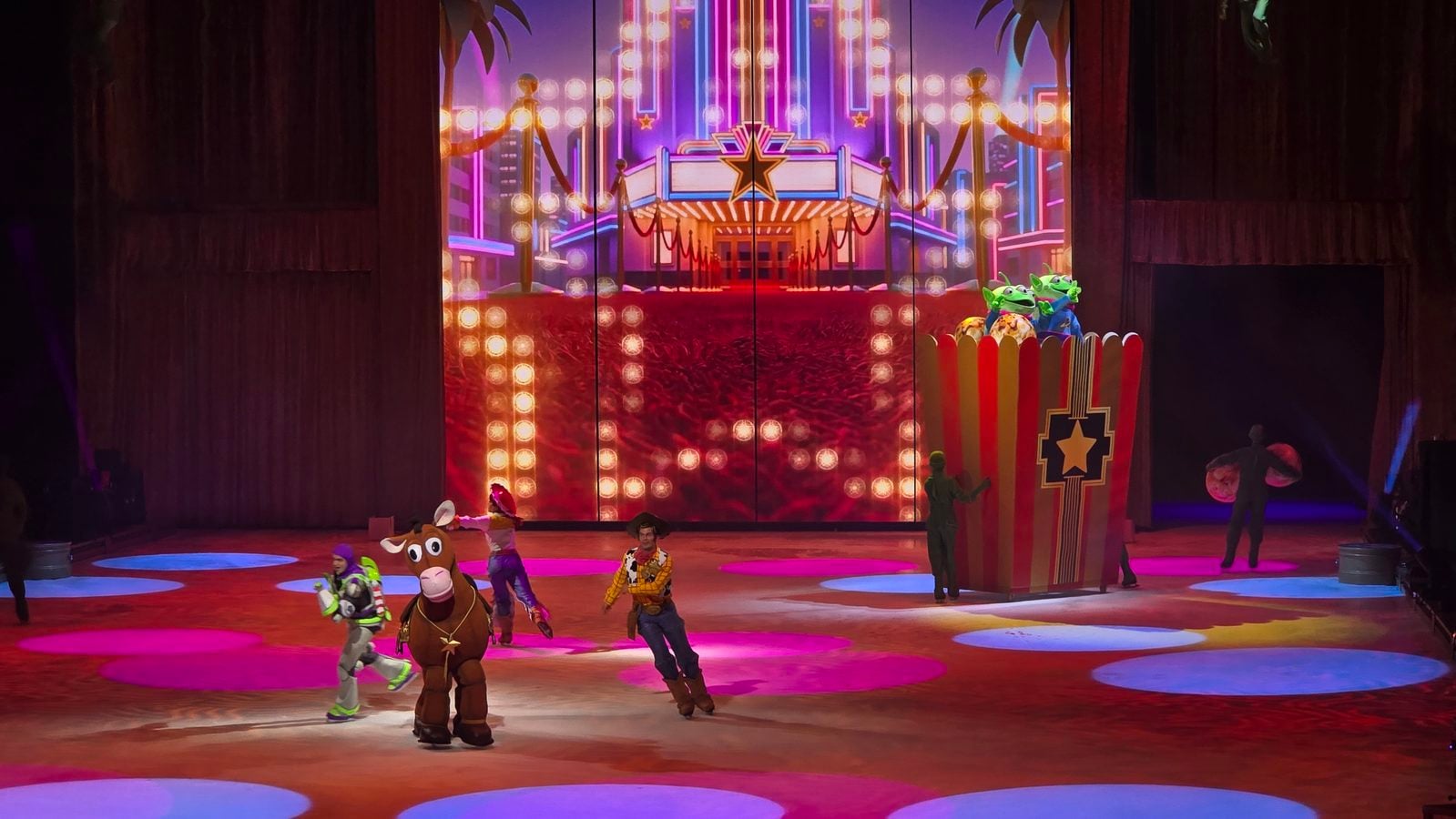Colorful ice skating stage with neon lights and a star entrance performers in animal and cowboy costumes skate on a lit rink