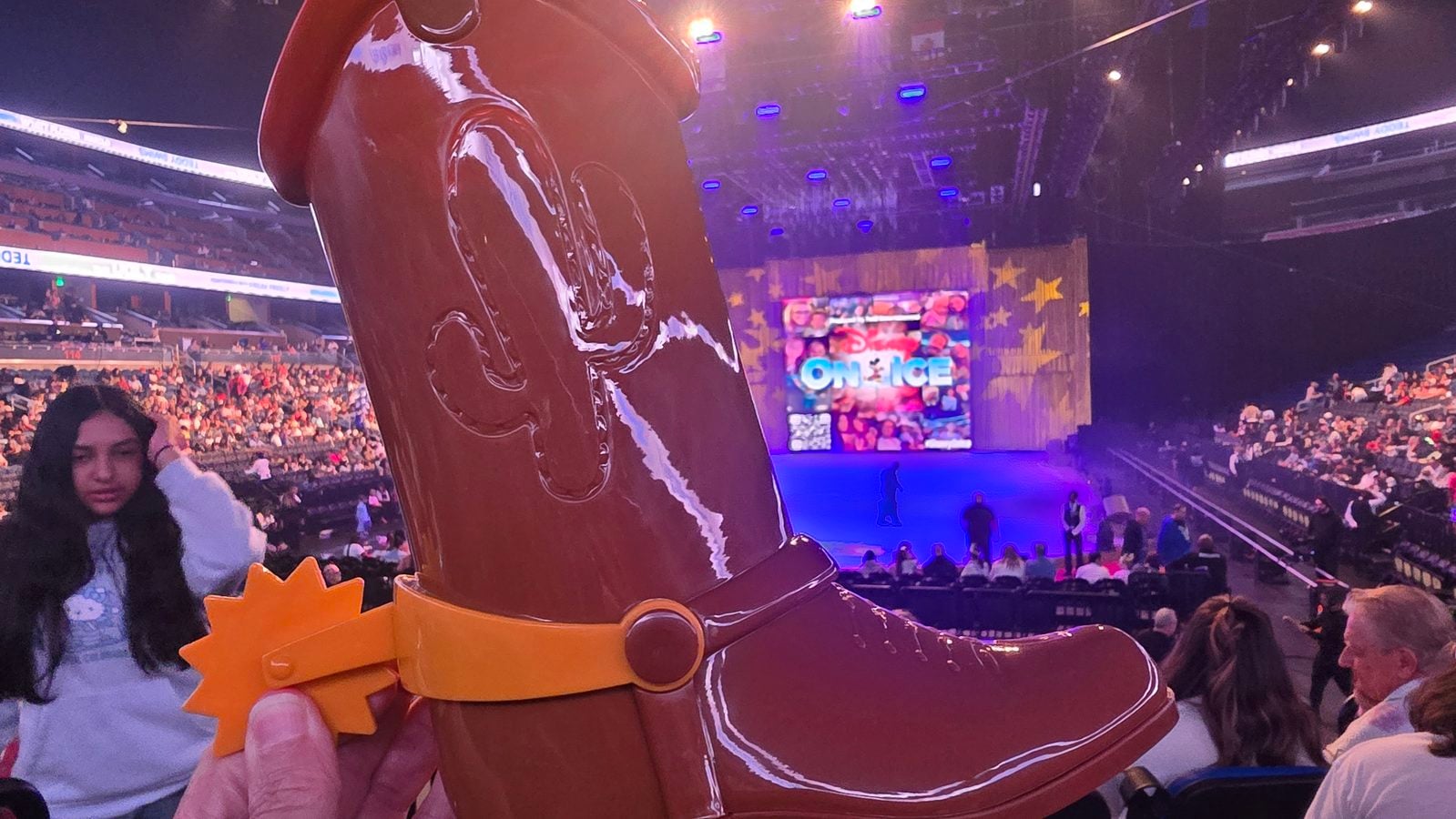 Close up of a giant glossy brown boot prop high above a crowded arena audience with a colorful stage in the background