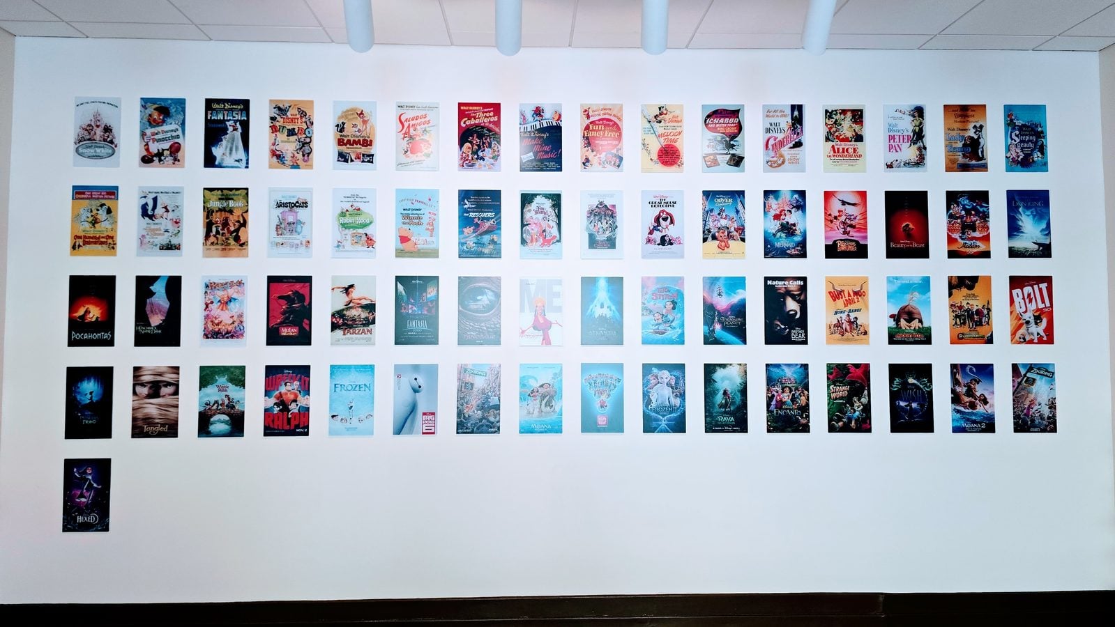 White gallery wall with dozens of small colorful movie posters arranged in a grid in several rows and columns