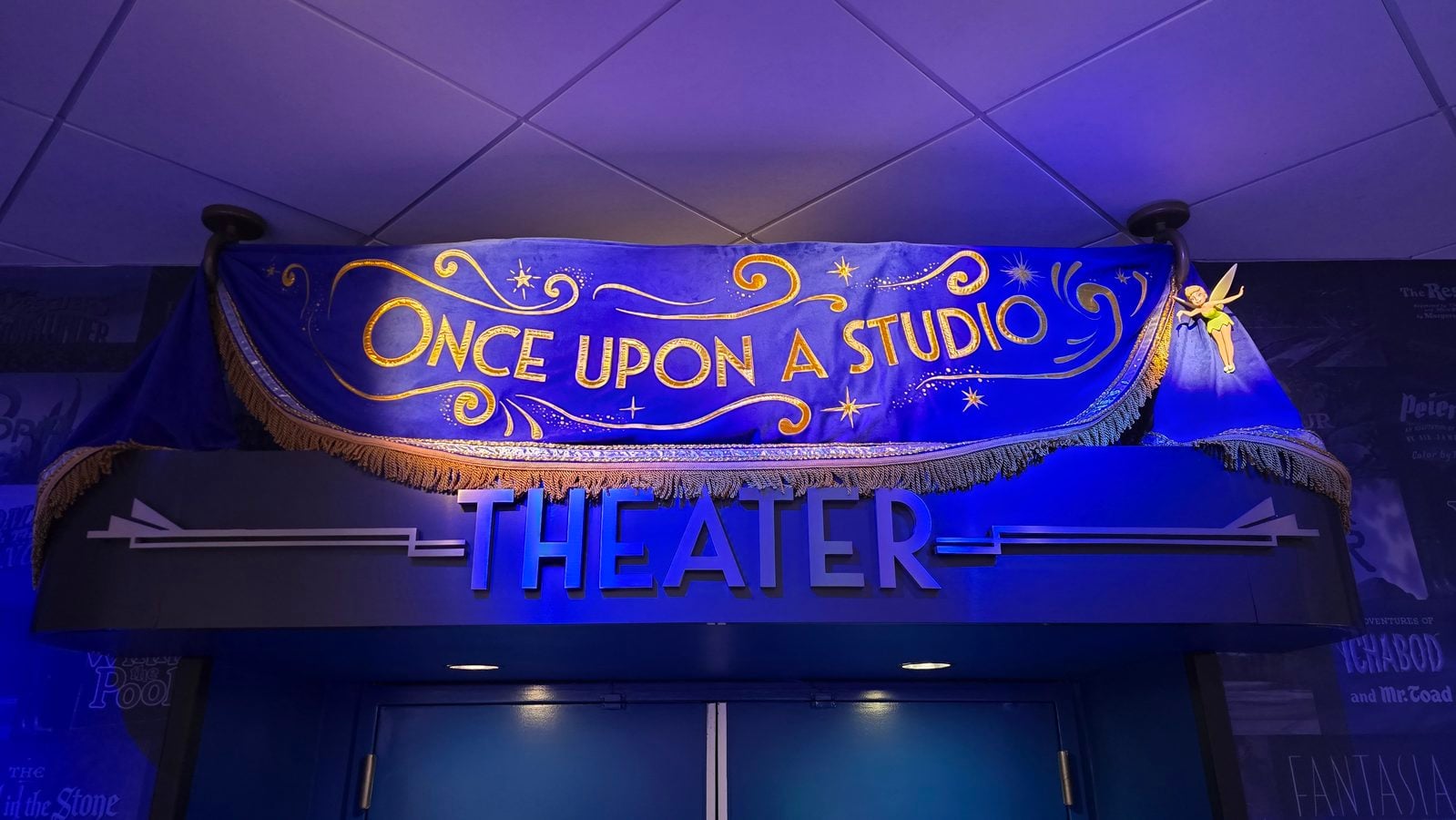 Blue banner reading Once Upon a Studio with gold lettering and decorative swirls hanging above theater doors