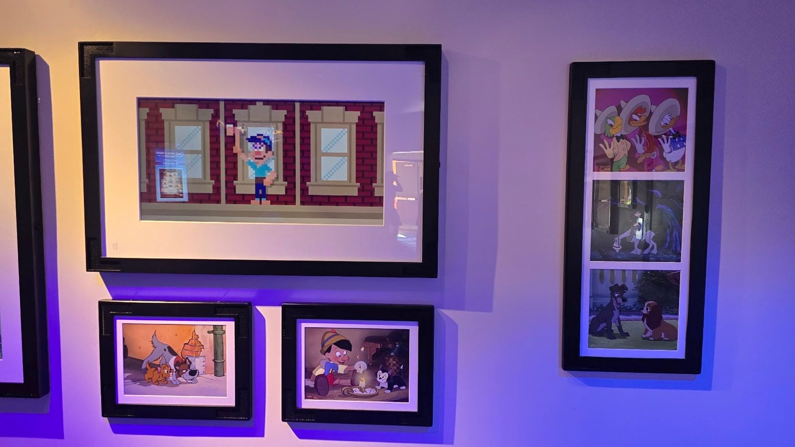 Gallery wall with multiple black framed cartoon prints under purple lighting