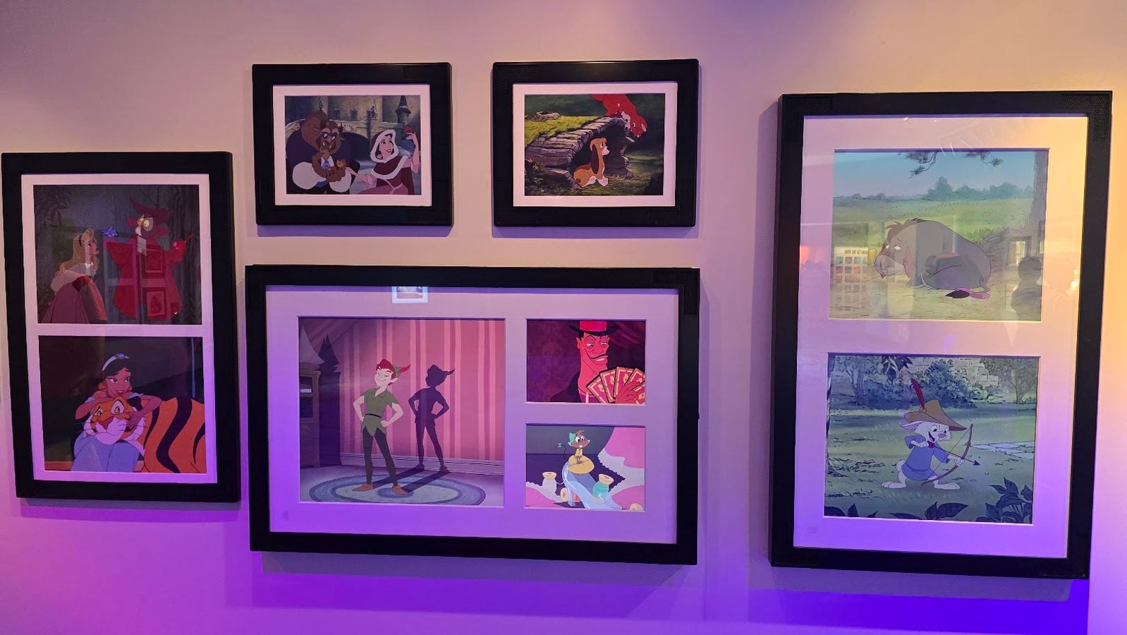 Wall mounted collage of framed Disney style cartoon scenes arranged in a grid on a purple lit wall