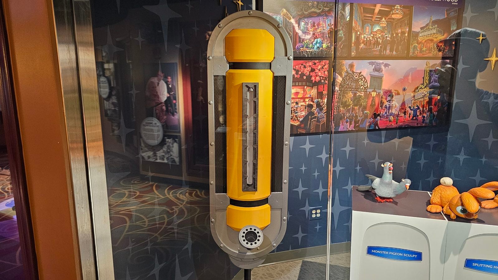 Yellow and gray vertical control unit mounted in a display case with colorful themed panels in the background artifact in a museumattraction display