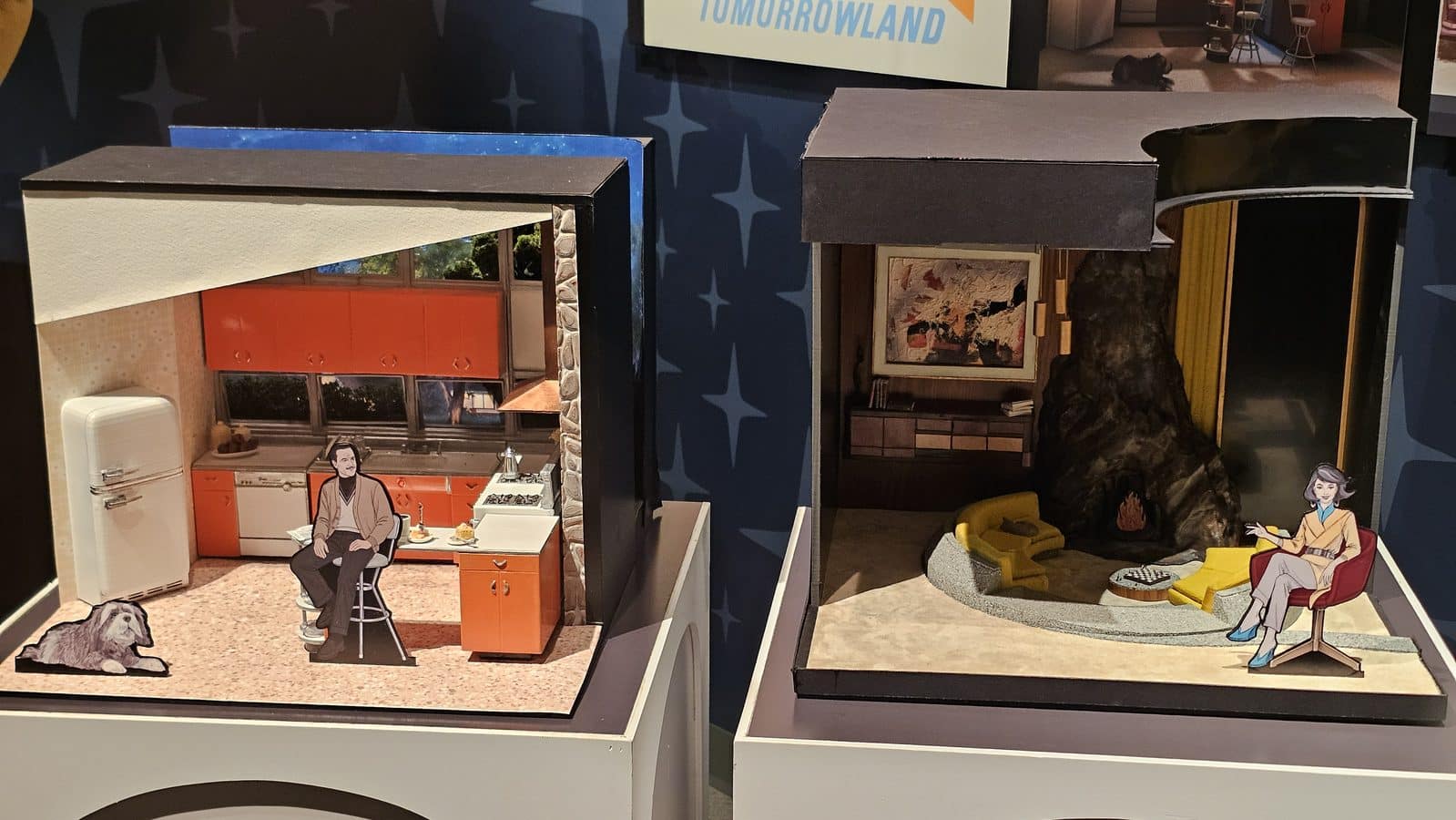 Two vintage style diorama rooms side by side left shows an orange kitchen with a retro fridge and cabinets a man sitting at a table and a dog on the floor right shows a living area with a fireplace rocking rock and a woman seated in a yellow chair
