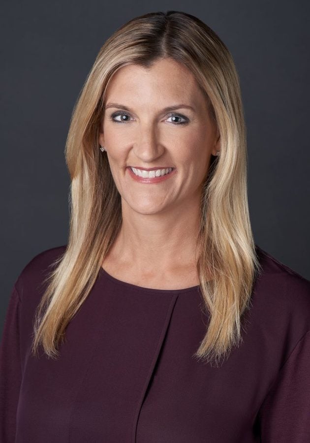 Smiling woman with shoulder length blonde hair in a burgundy blouse against a dark gray background