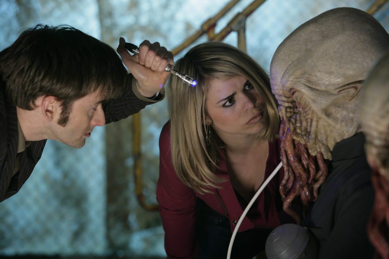 Three people lean in closely examining a lifesize skeleton prop with a small flashlight in a dim workshoplike setting
