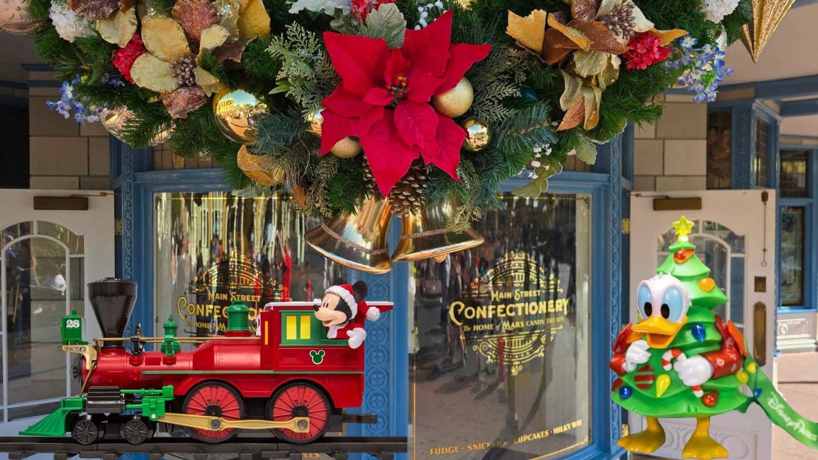 Festive storefront display with a red toy train featuring Mickey in a Santa hat a large red poinsettia centerpiece gold bells and holiday greenery outside a confectionery shop
