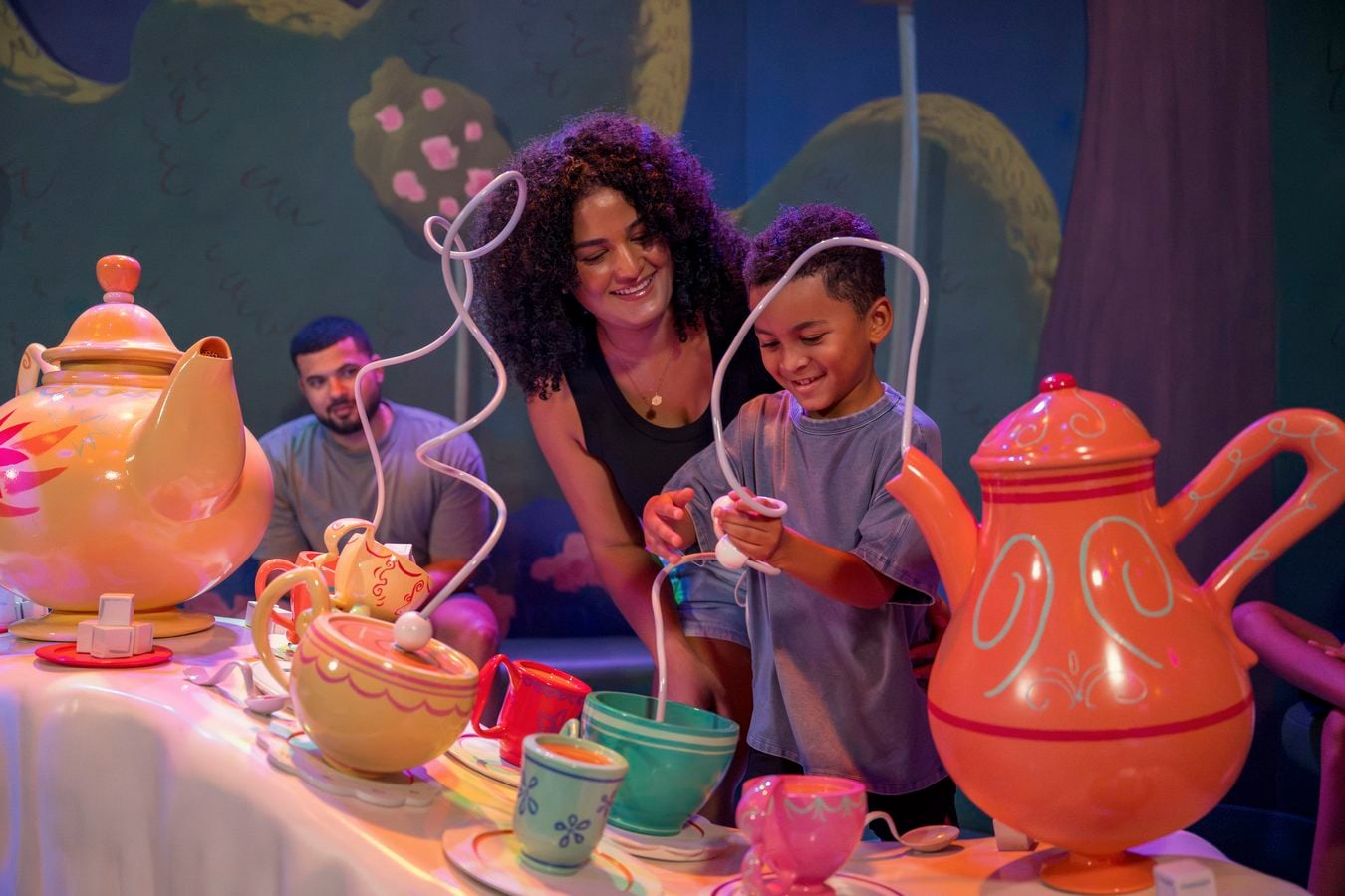 Mother and child smiling as they play a whimsical tea party with colorful oversized teapots and cups at a themed exhibit