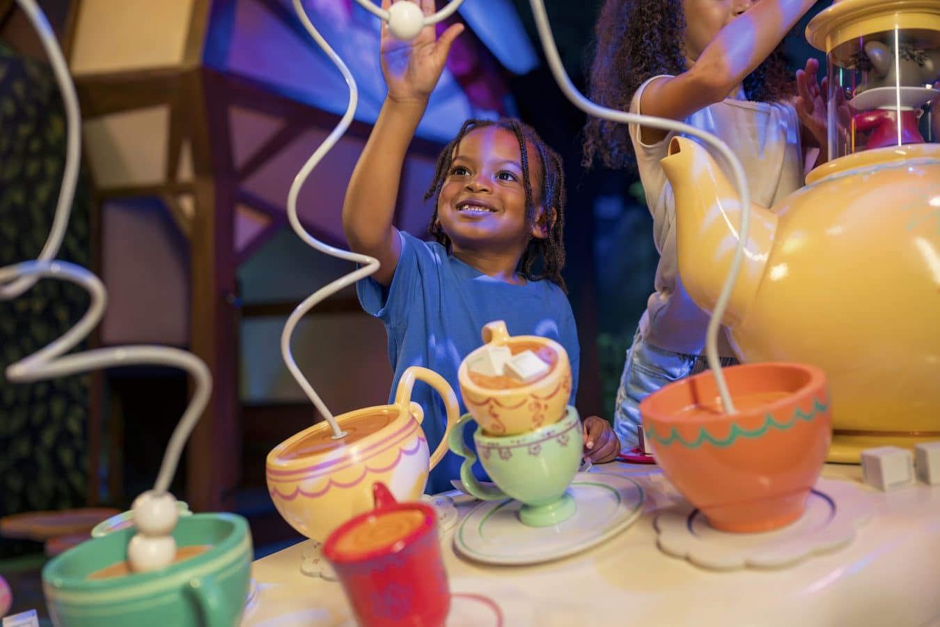 Children at a colorful tea party with stacked teacups and teapots on a bright table