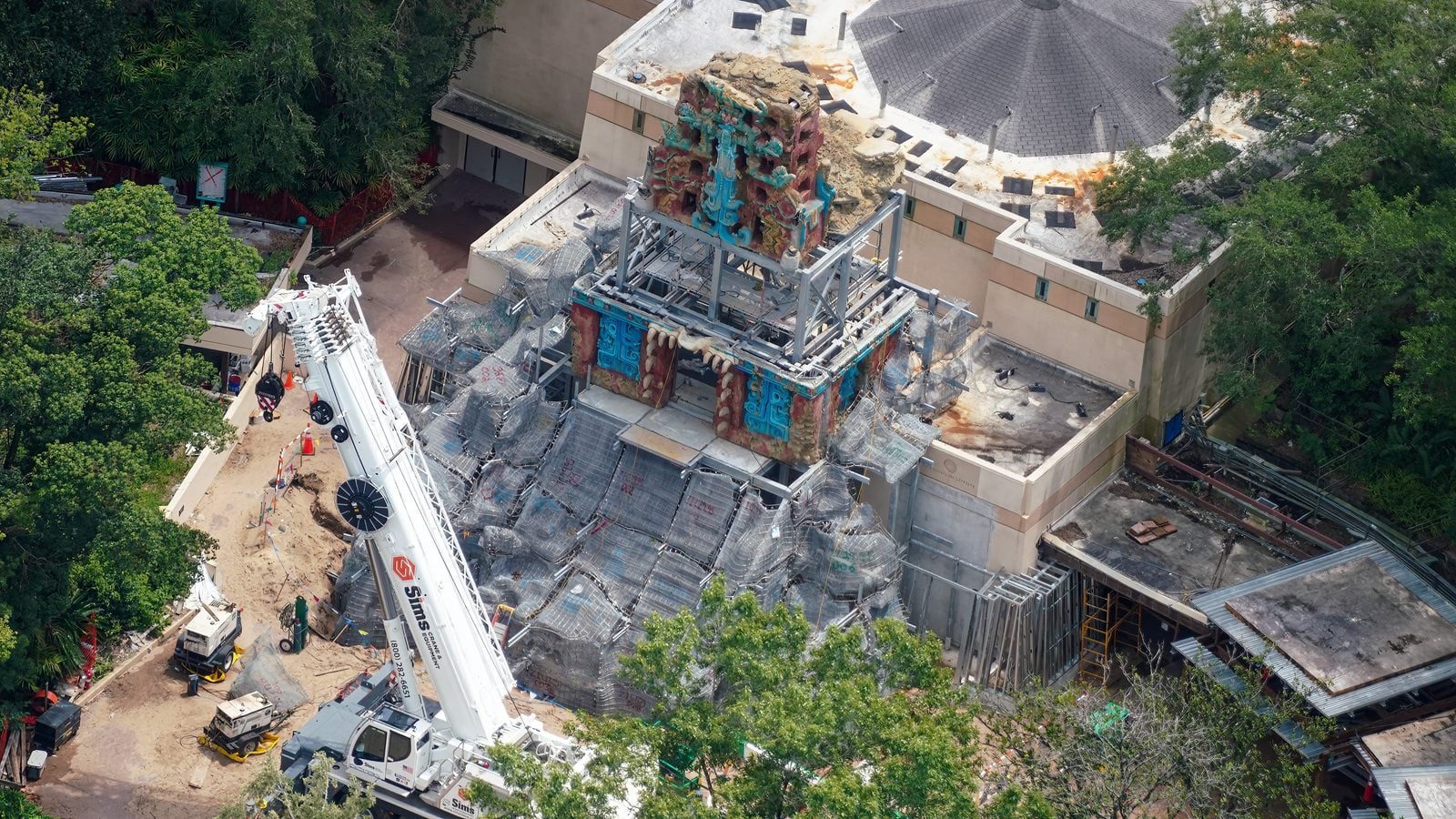 Aerial view of a temple like structure under construction with colorful sculpted decorations scaffolding and a tall crane nearby
