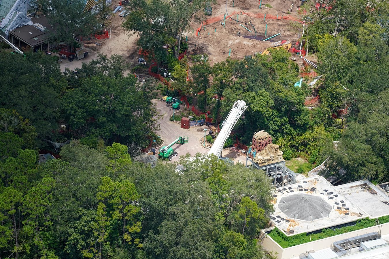 Aerial view of a construction site surrounded by trees with excavated dirt orange safety fencing and machinery
