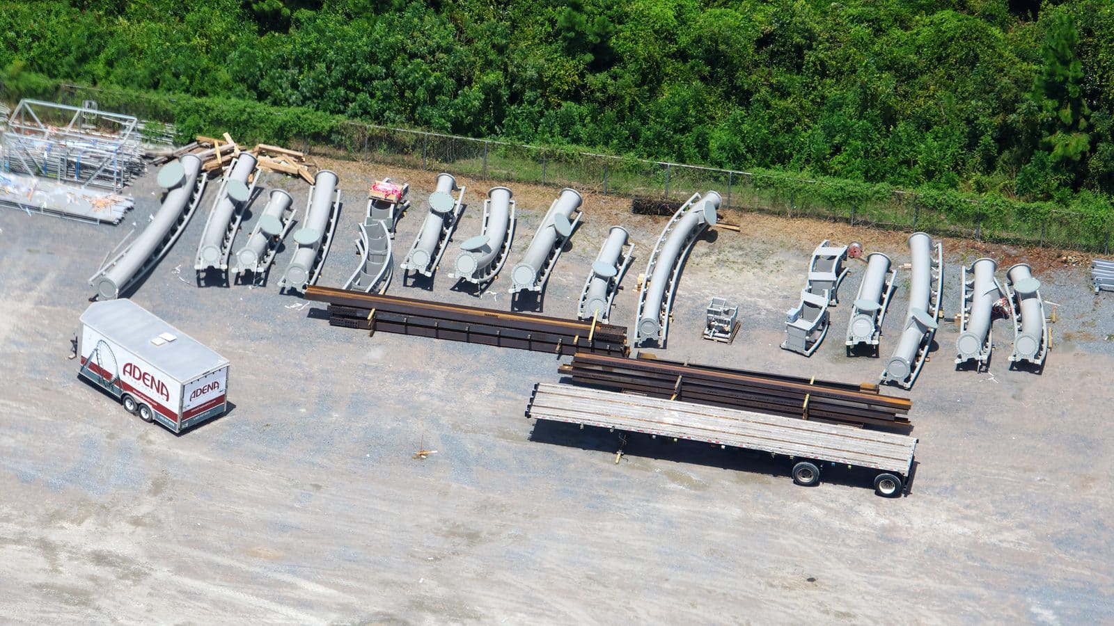 Aerial view of a construction yard with curved gray metal pipes and stacked beams on gravel