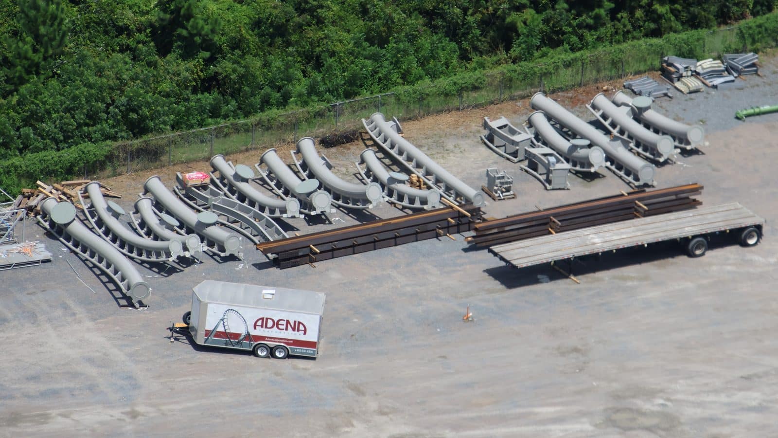 Large outdoor storage yard with rows of curved gray pipes and a white ADENA trailer in the foreground