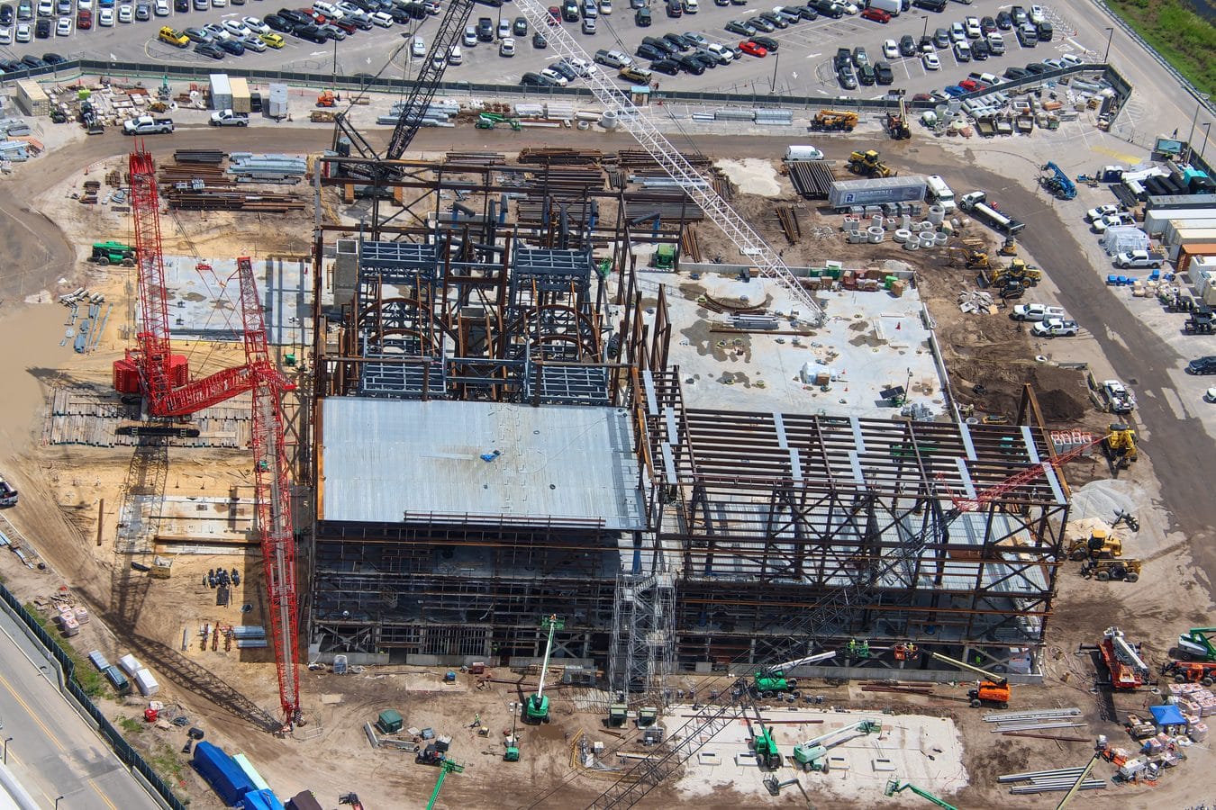 Aerial view of a large construction site with a steel framework red and white cranes and piles of pipes and materials scattered around