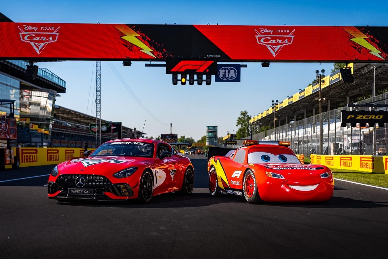 Two red race cars on a track under a large Disney Pixar Cars banner with Pirelli barriers in view